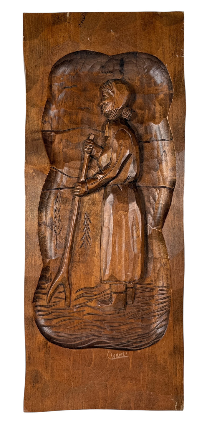 Wooden relief sculpture of a figure holding a child, with intricate details on a wooden panel.