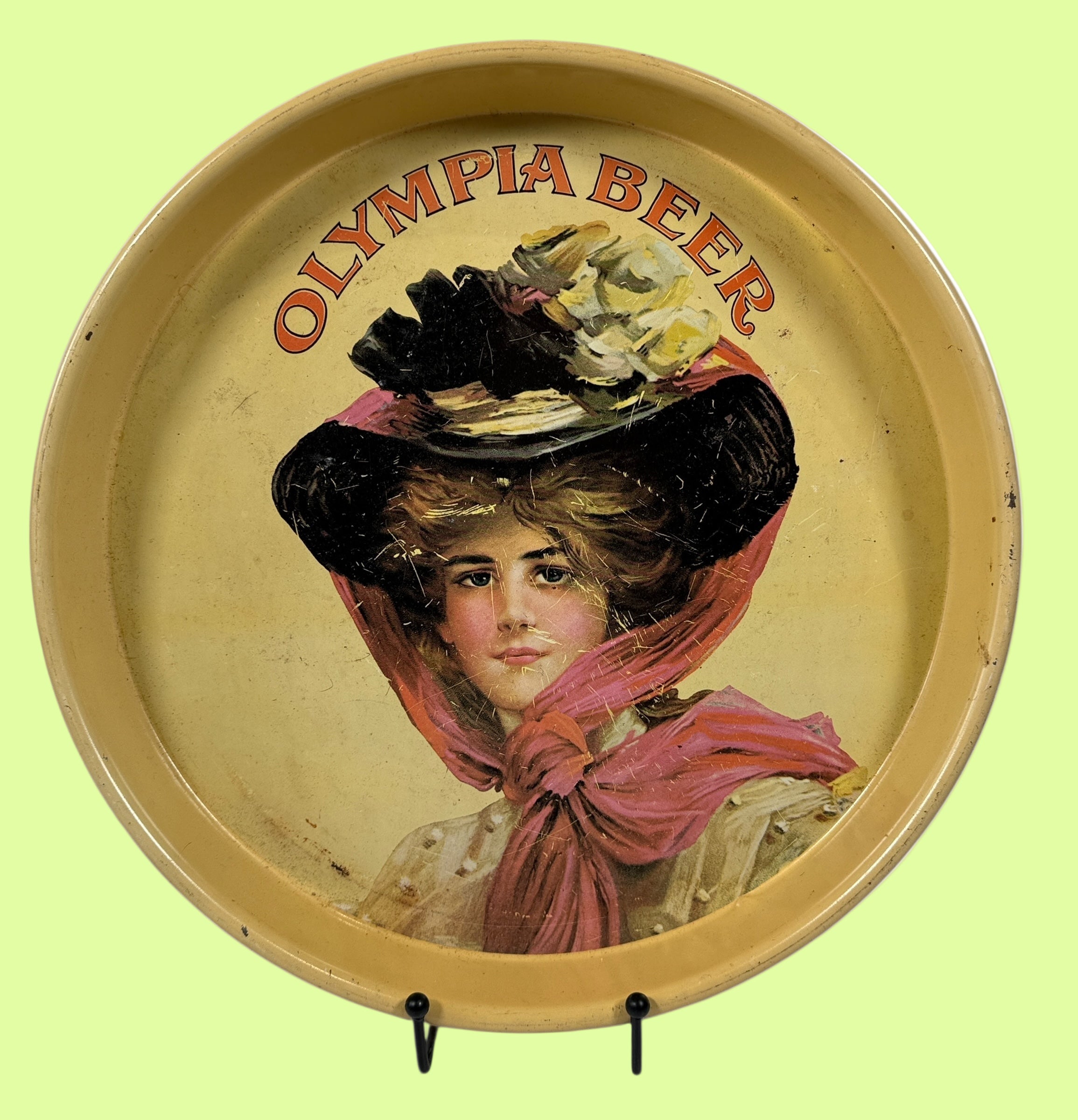 Round tray with vintage illustration of a woman wearing a large hat and scarf, and 'Olympia Beer' text.