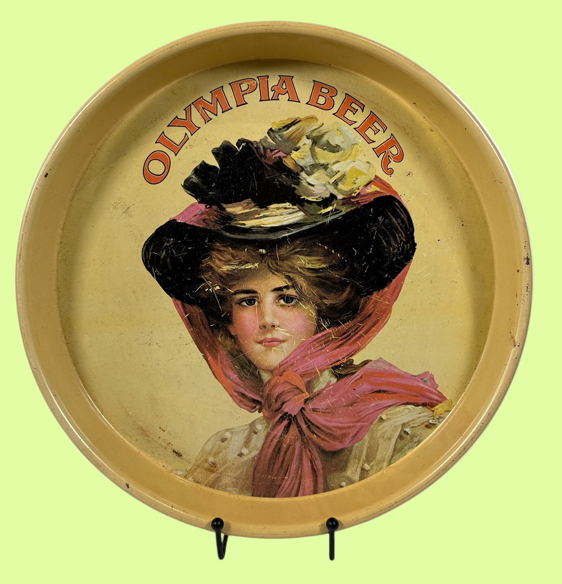 Round tray with vintage illustration of a woman wearing a large hat and scarf, and 'Olympia Beer' text.