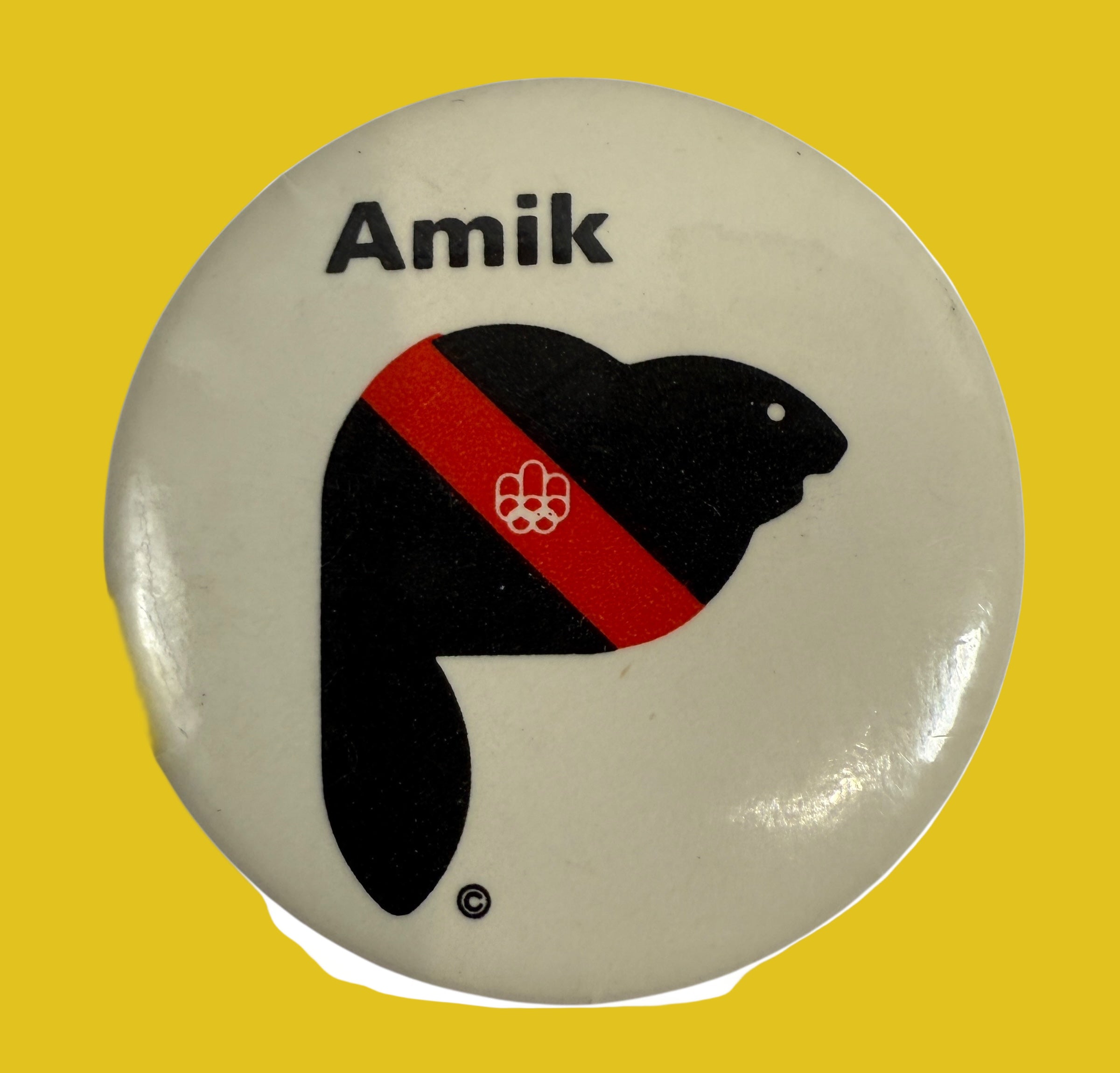 Button badge with a black silhouette of a beaver, red stripe, and 'Amik' text on a beige background