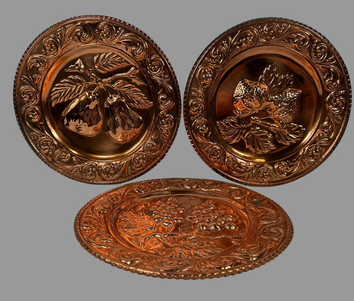 Three copper plates with intricate designs on a white background