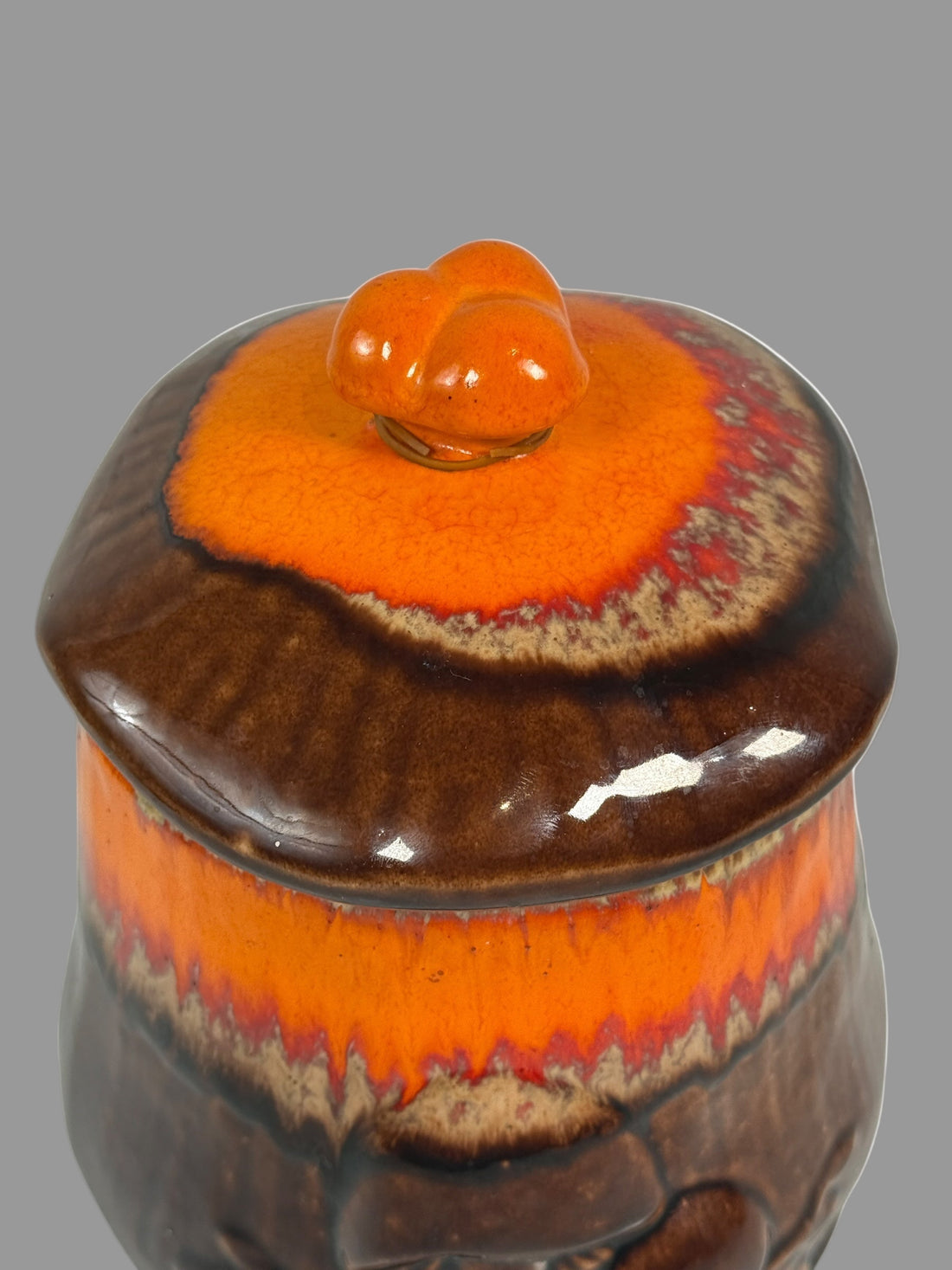 Ceramic jar with a lid featuring orange and brown glaze on a white background