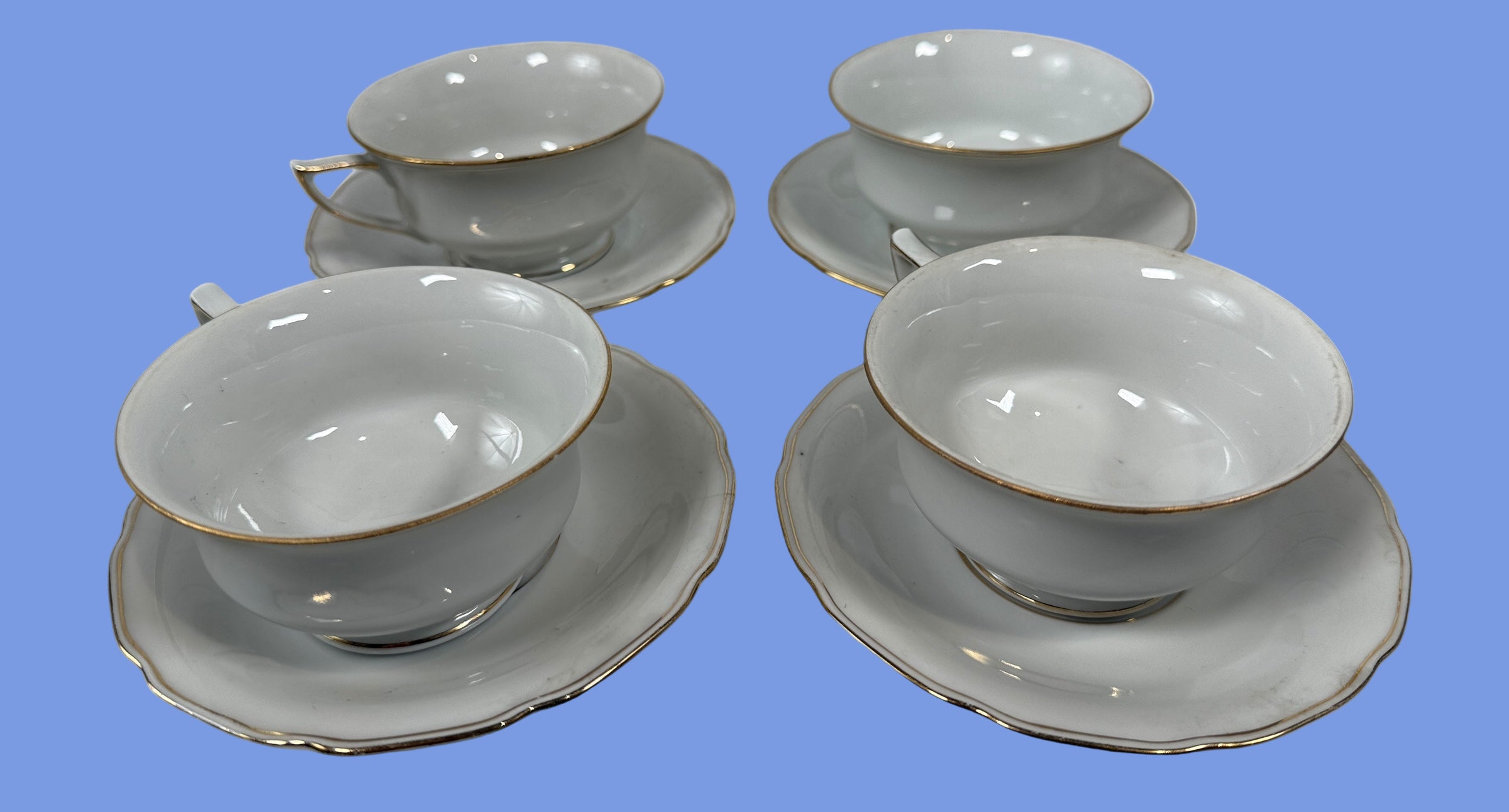 Set of four white ceramic tea cups and saucers with gold rims on a white background