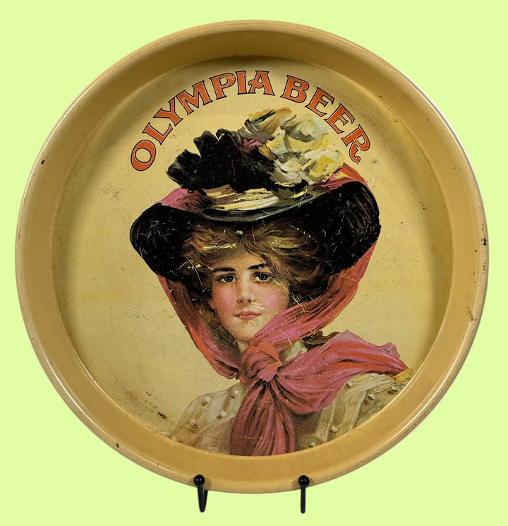 Round tray with a vintage illustration of a woman wearing a large hat and scarf, with 'Olympia Beer' text above.