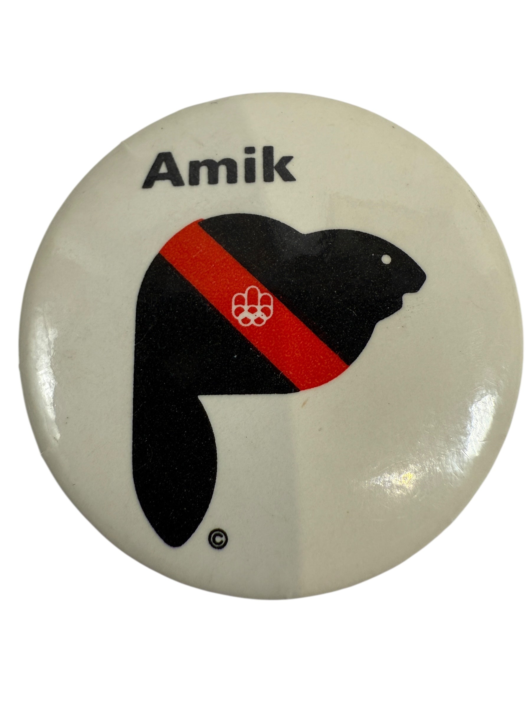 1976 Olympic Button badge with 'Amik' text and black silhouette of a beaver with a red stripe on a white background