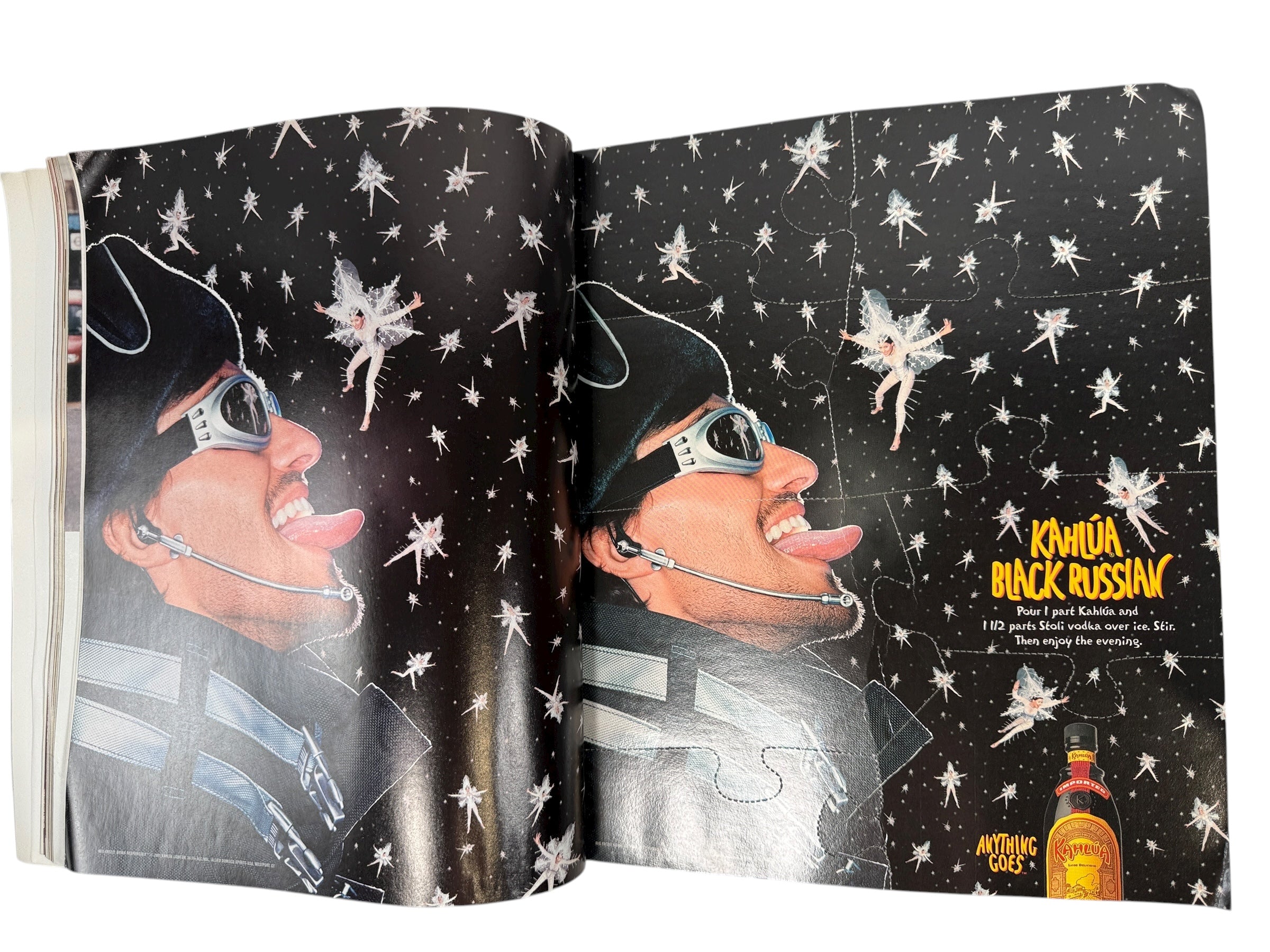 Open book with a black and white illustration of a person wearing sunglasses and a hat, with fairy graphics on a starry background. Kahláu Black Russian branding is visible.
