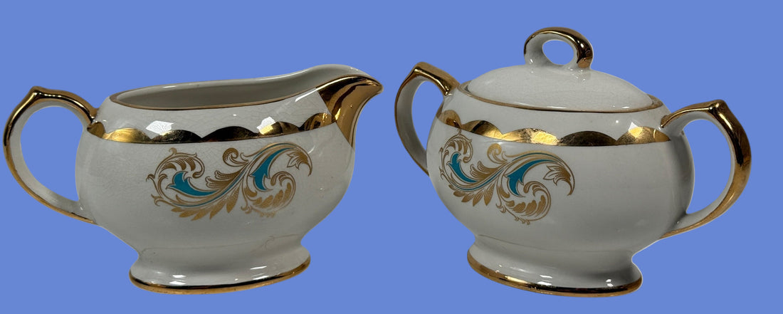 Two ceramic creamer and sugar bowl set with gold and blue floral patterns on a white background