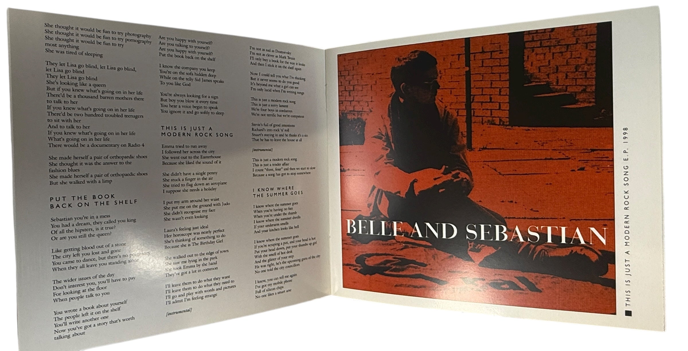 Open book with text on one side and a cover illustration of a person playing guitar on the other, featuring the band 'Belle and Sebastian'.