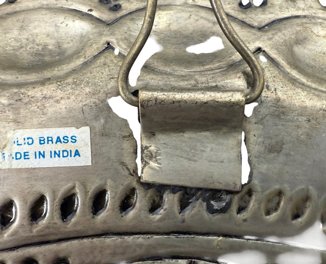 Metallic object with decorative patterns and a label indicating 'Solid Brass Made in India'.