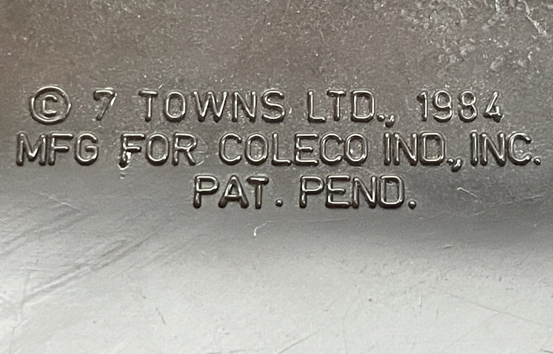 Metallic surface with embossed text '© 7 Towns Ltd. 1984 MFG FOR COLECO IND., INC. PAT. PEND.'