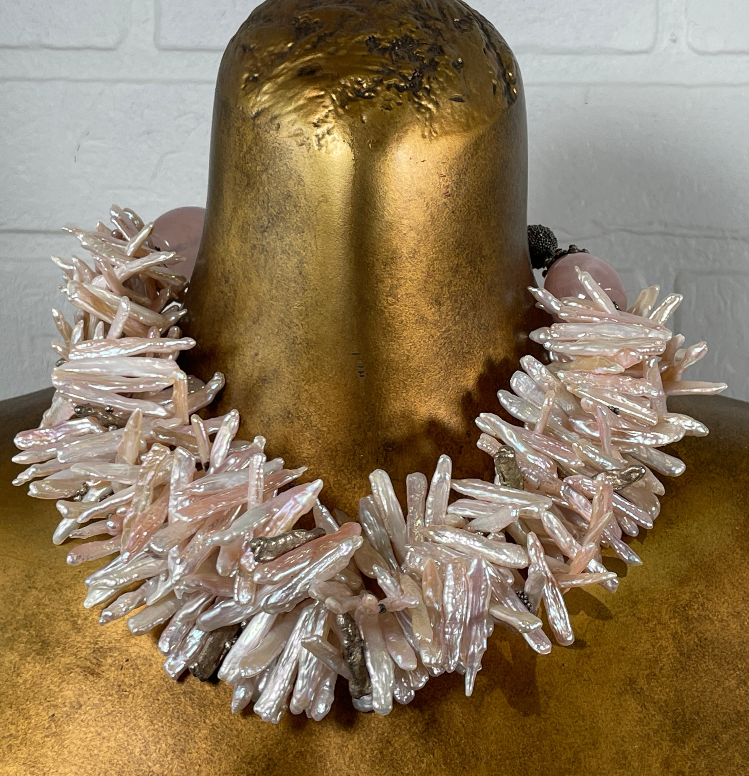 Necklace with crystal-like stones worn by a person with gold-painted hair against a white brick wall.
Baroque_Pearl_Necklace 