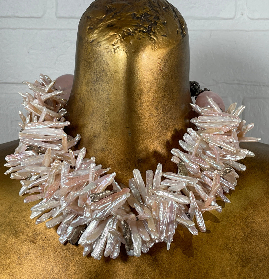 Necklace with crystal-like stones worn by a person with gold-painted hair against a white brick wall.
Baroque_Pearl_Necklace 