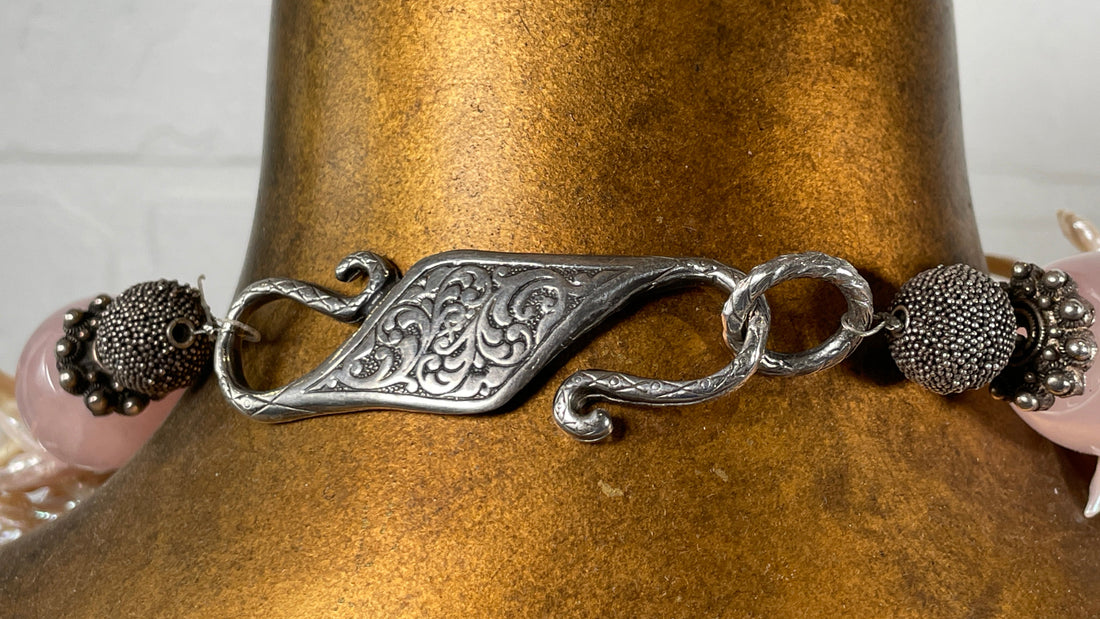 Silver bracelet with intricate design on a bronze mannequin against a white brick wall.