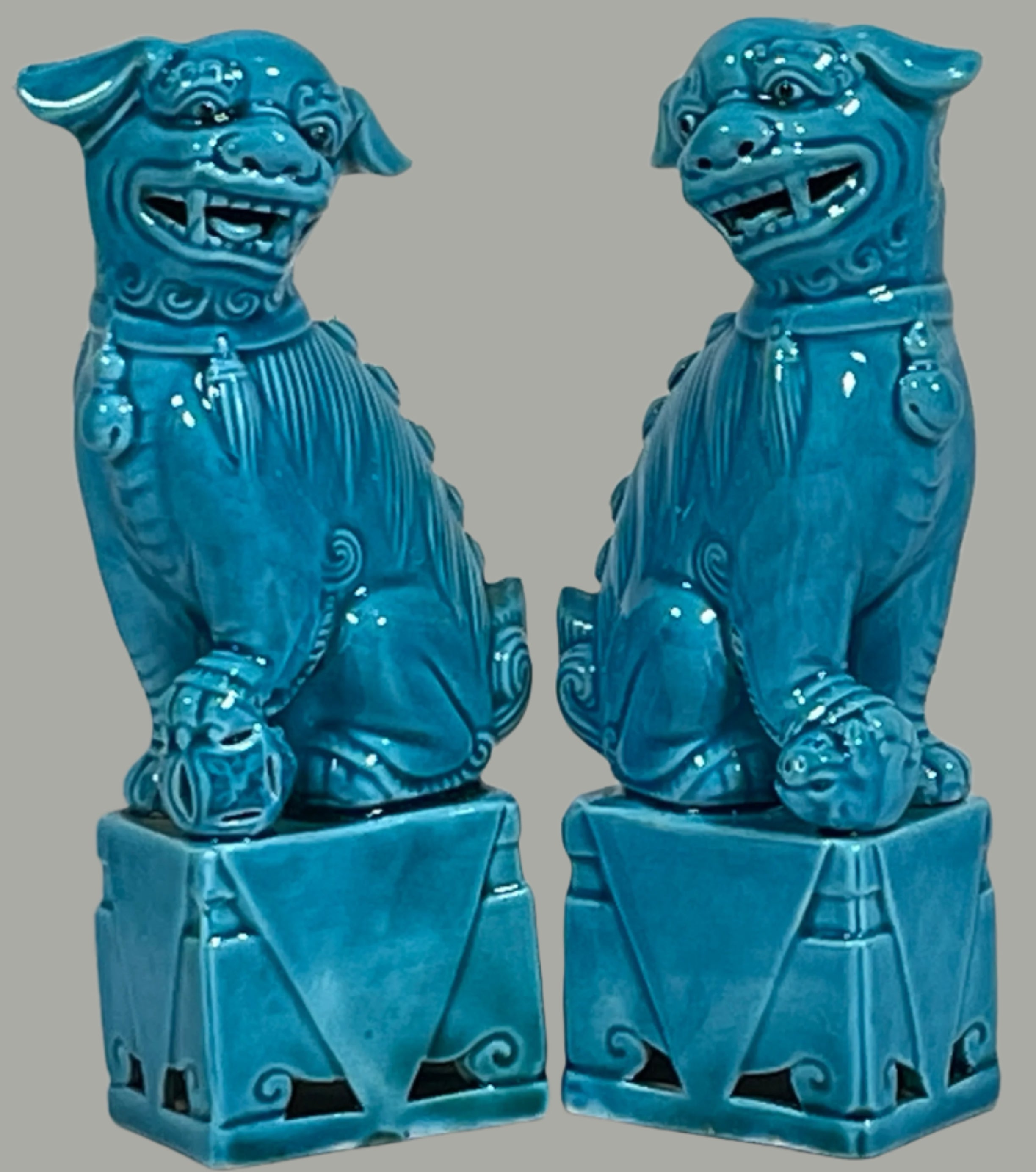 Pair of blue ceramic dog statues on a white surface with a light gray brick wall background.