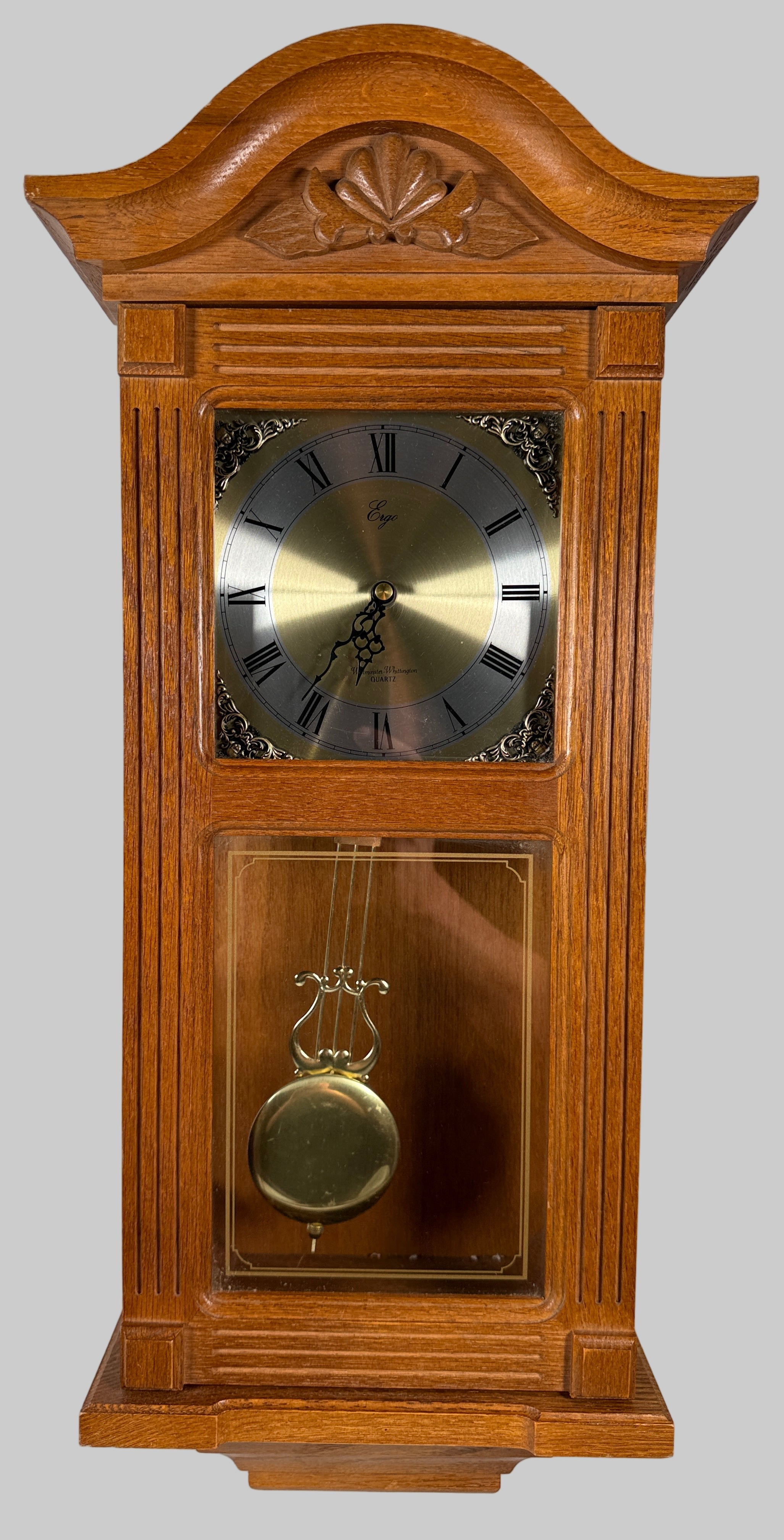 Wooden grandfather clock with pendulum against a white brick wall.