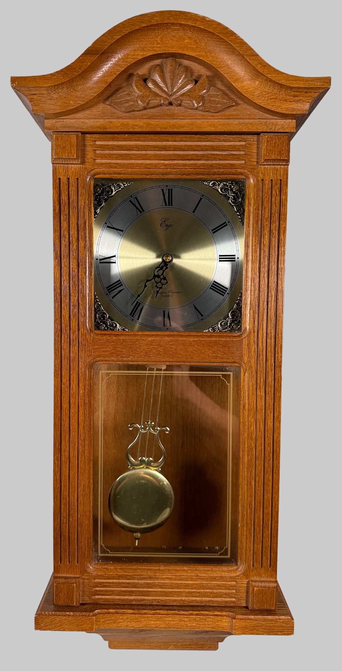 Wooden grandfather clock with pendulum against a white brick wall.