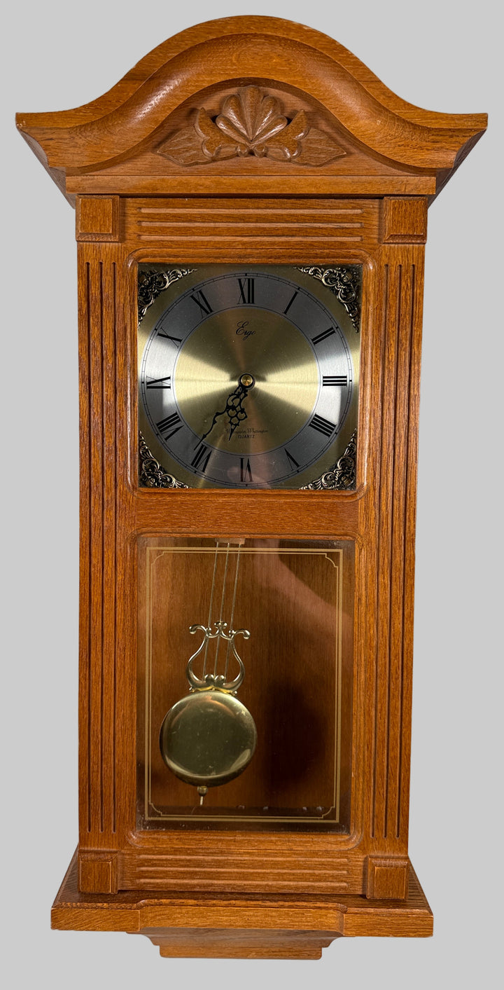 Wooden grandfather clock with pendulum against a white brick wall.