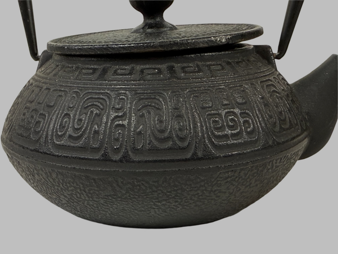 Black cast iron teapot with intricate designs on a white background