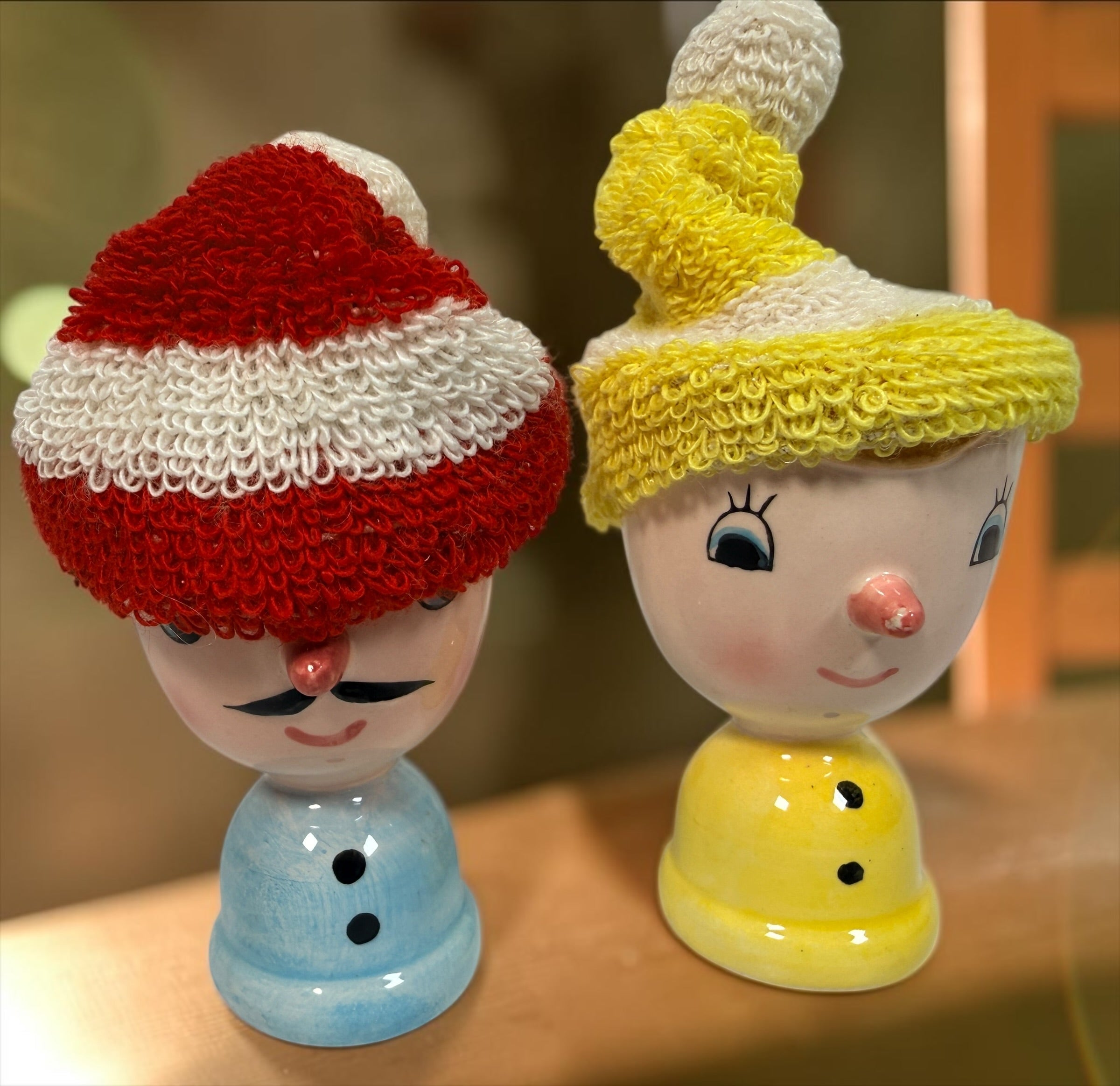 Vintage Japanese ceramic boy and girl egg cups with original colourful yarn egg cozy hats. Charming 1960s–70s novelty kitchenware pair.