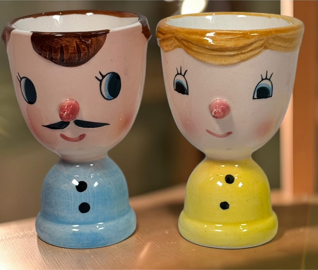 Vintage Japanese ceramic boy and girl egg cups with original colourful yarn egg cozy hats. Charming 1960s–70s novelty kitchenware pair.