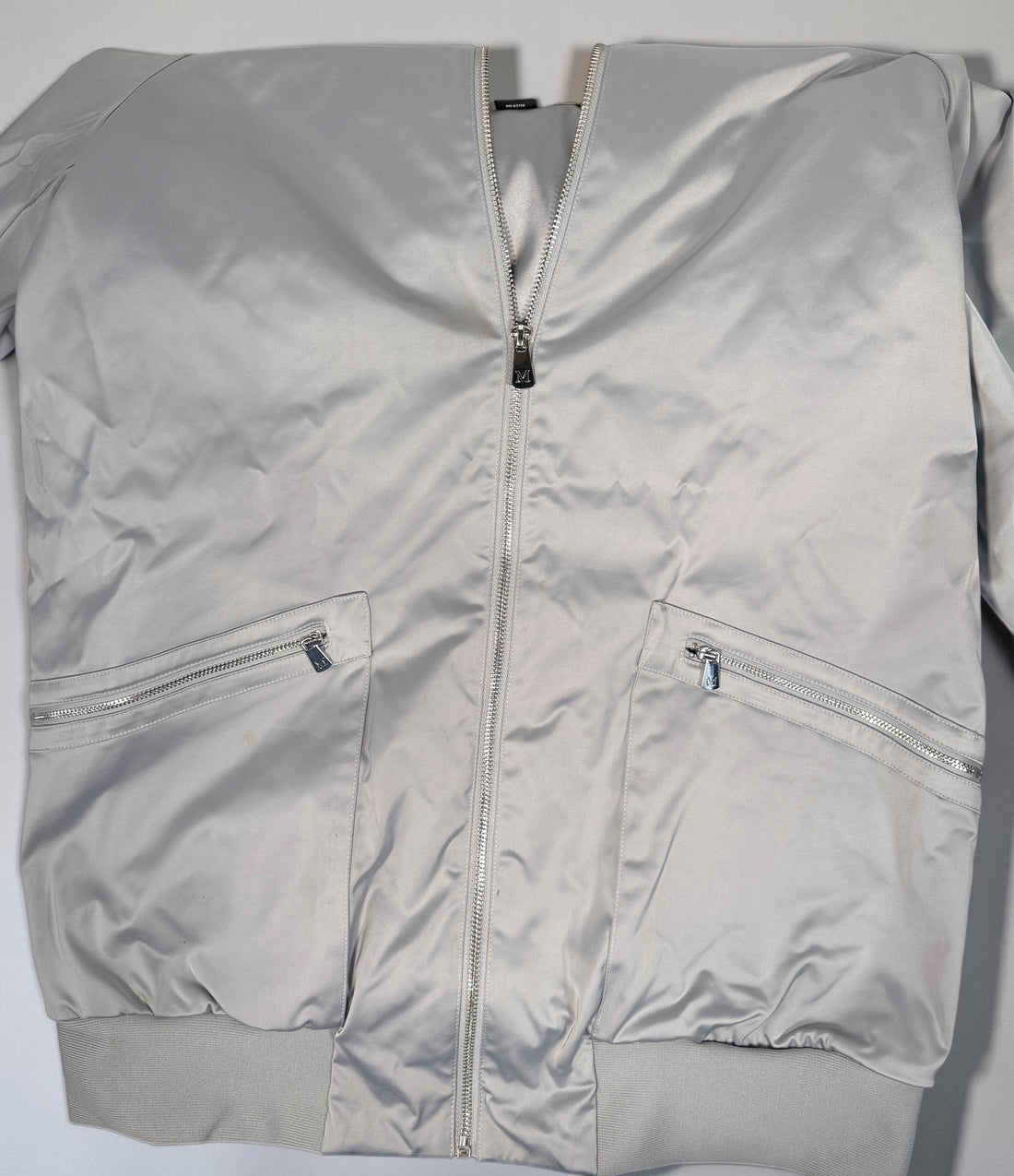 Shop the Marciano Limitless bomber jacket in silver-grey satin, size M. Original tags attached, zip pockets and ribbed trim. Minor marks disclosed.