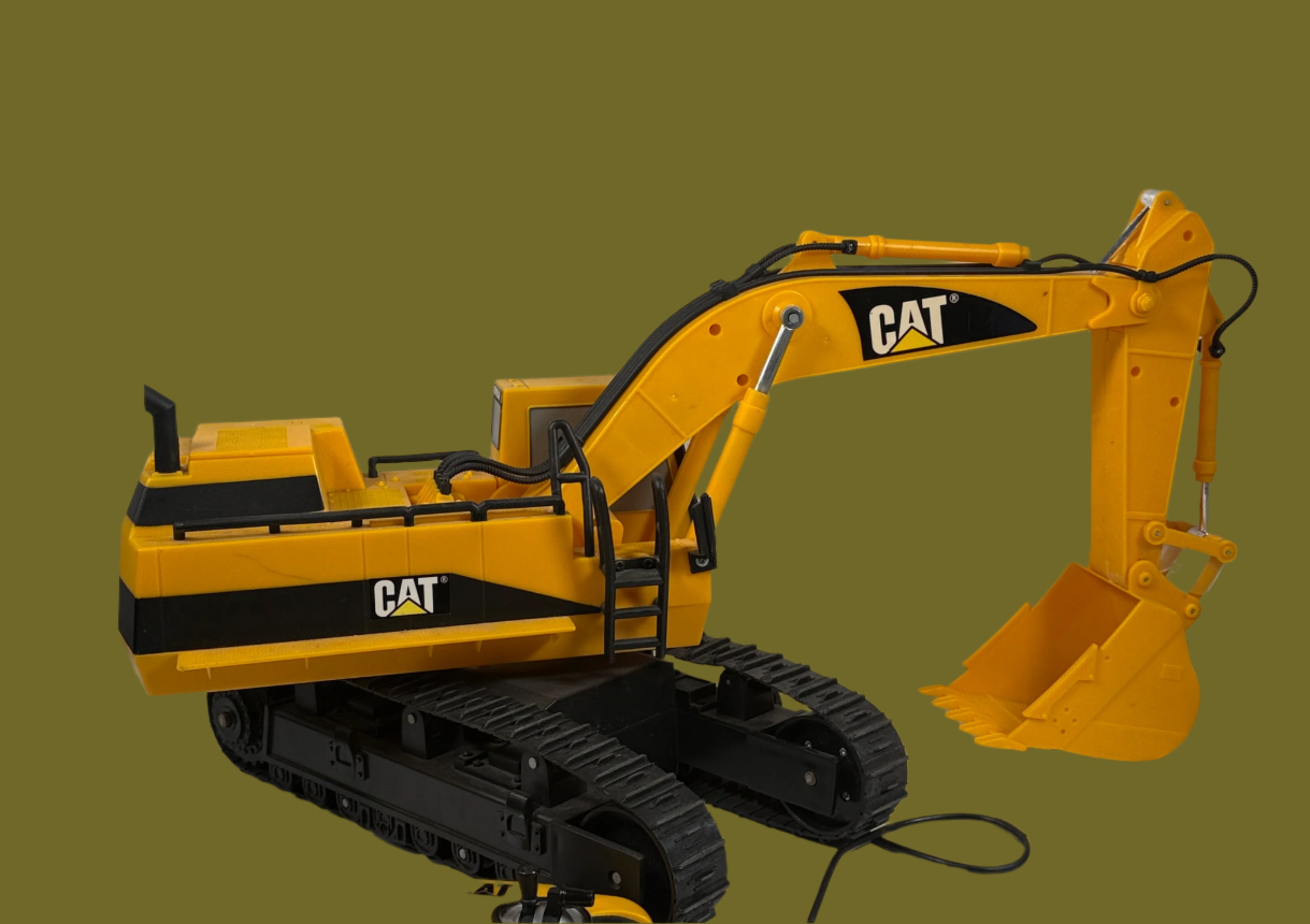 Yellow toy excavator with black tracks on a white surface against a light gray brick wall.