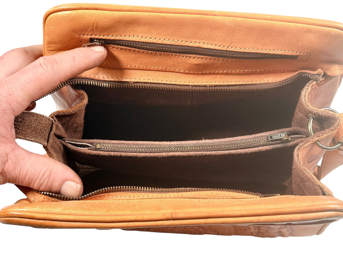 Brown leather handbag with a zipper being opened by a hand on a white background