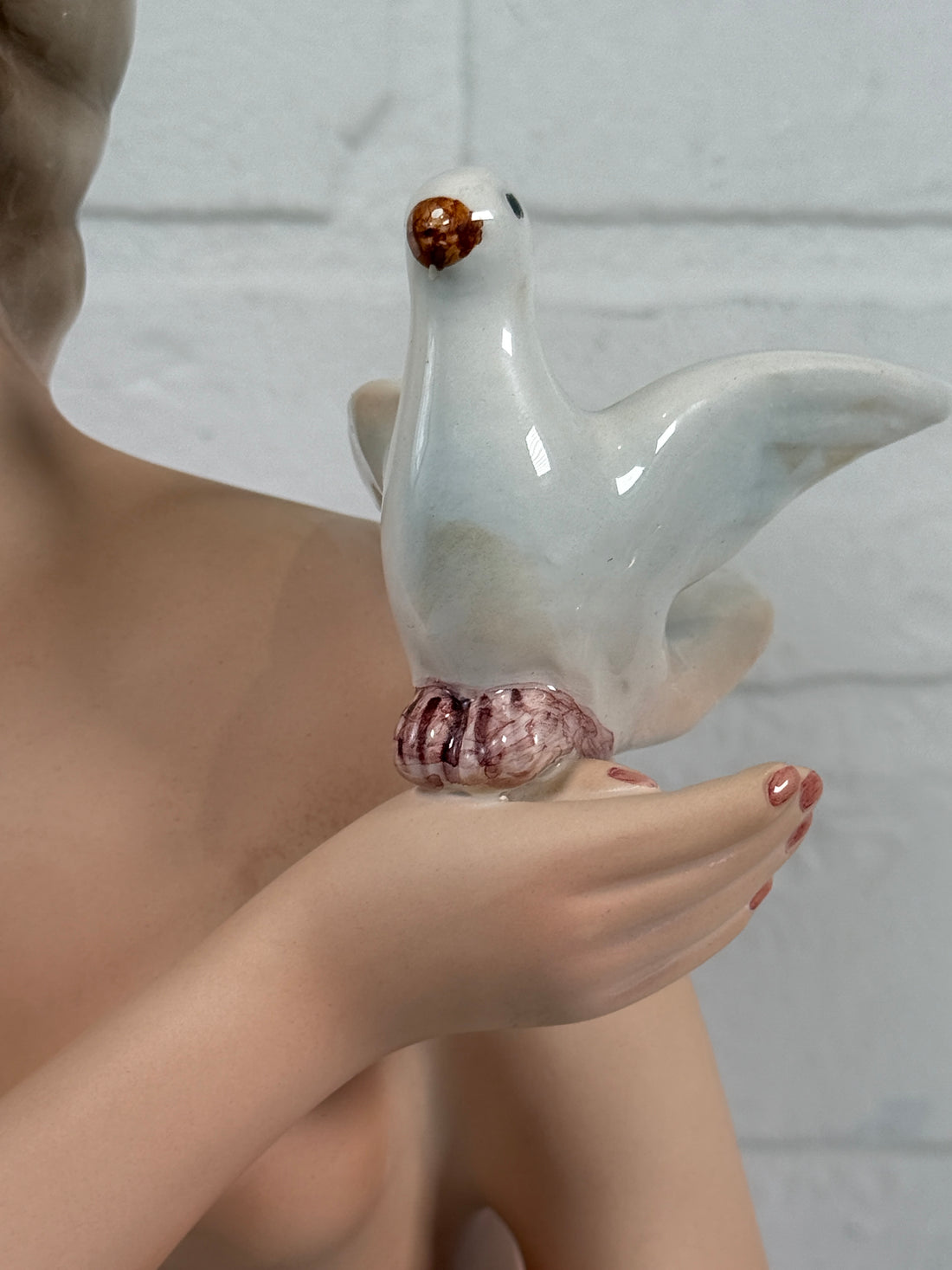 Hand holding a white ceramic teapot with a small brown object on a light gray background