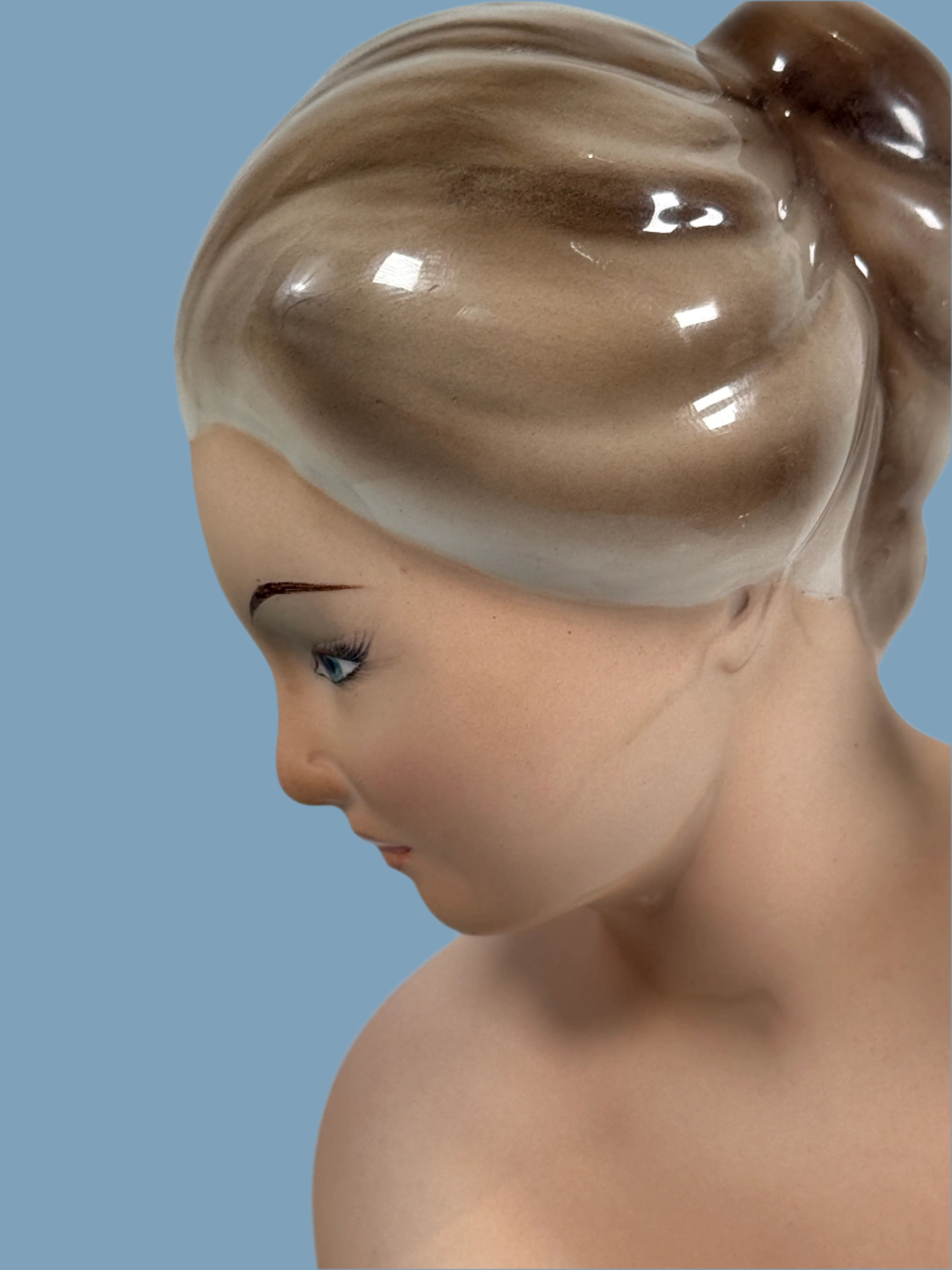 Close-up of a ceramic figurine with detailed hair and facial features on a plain background
