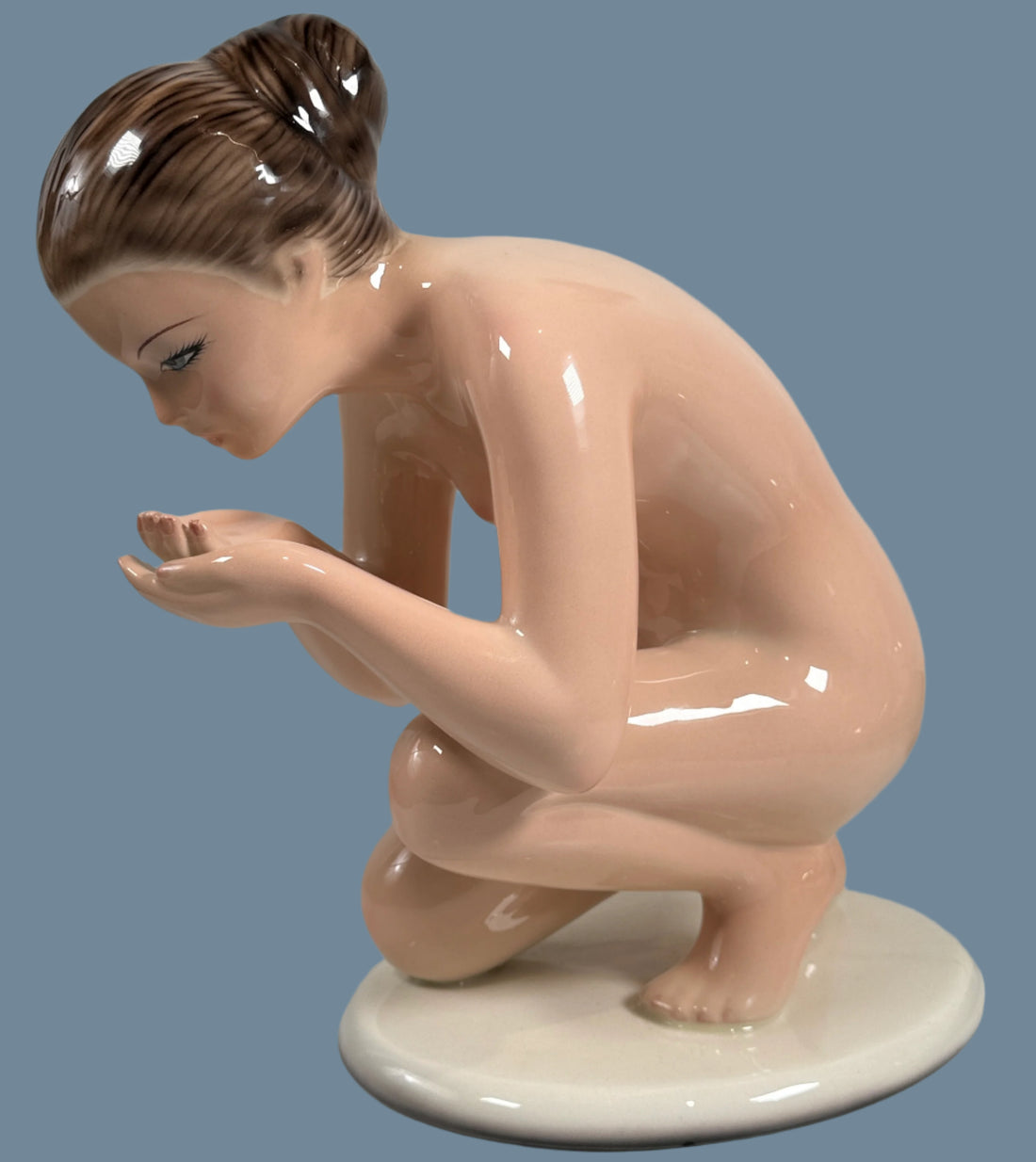 Porcelain figurine of a nude woman crouching on a white background