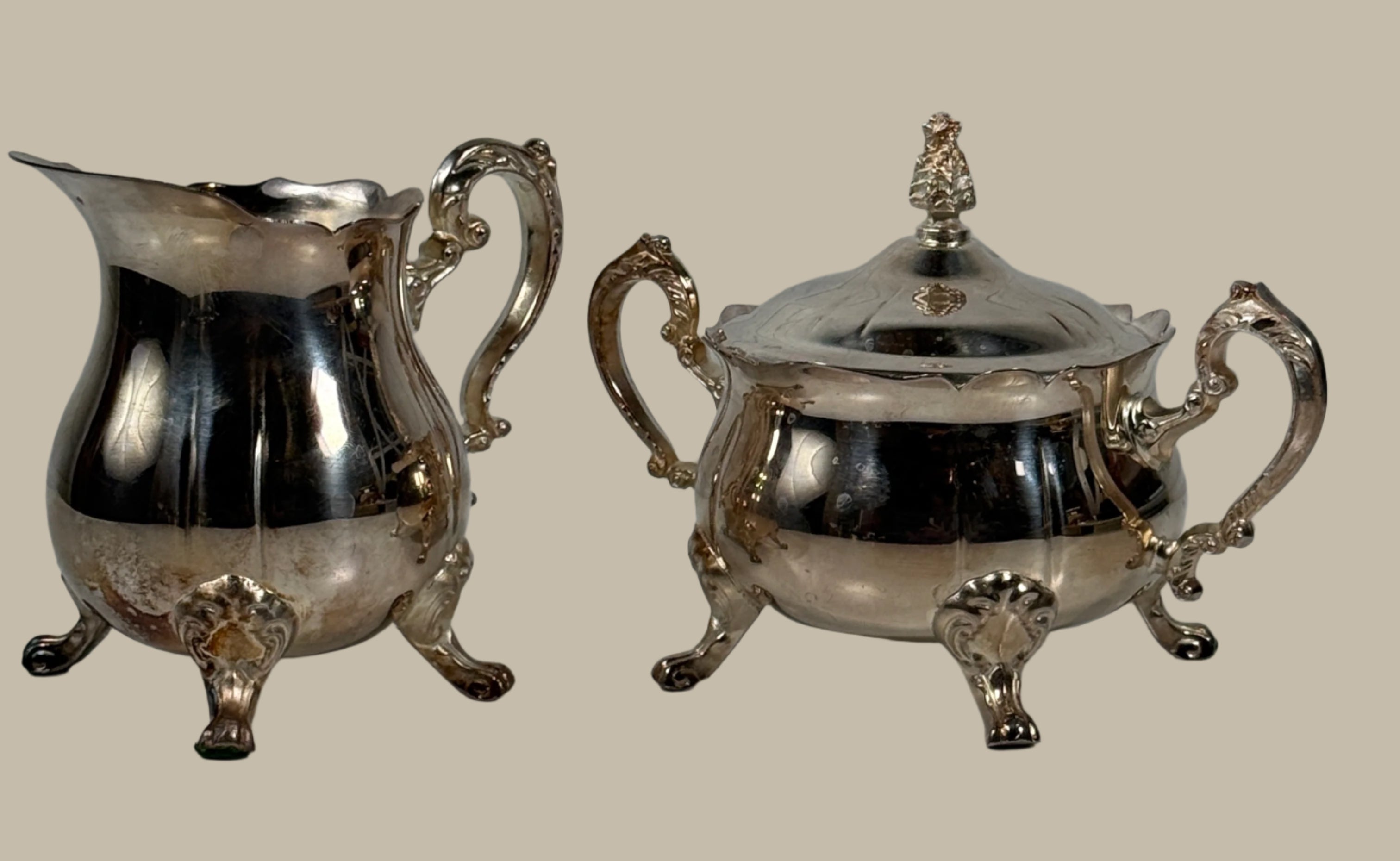 Silver creamer and sugar bowl set on a white surface with a light gray brick wall background.