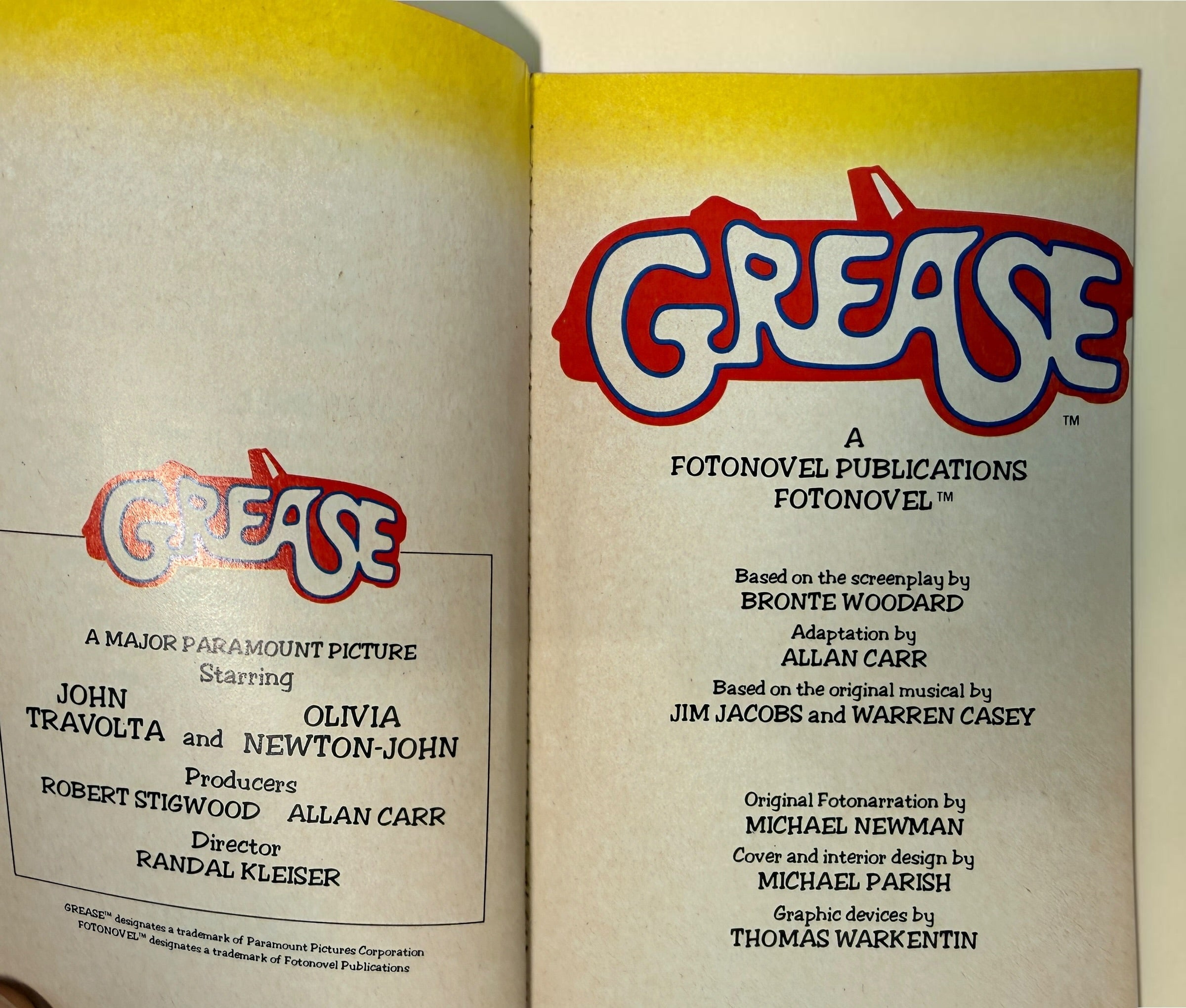 An open vintage book or booklet showing the title page for 'Grease,' with the title in large red, white, and blue lettering on both pages. Visible text includes production credits and 'A Fotonovel Publications Fotonovel.