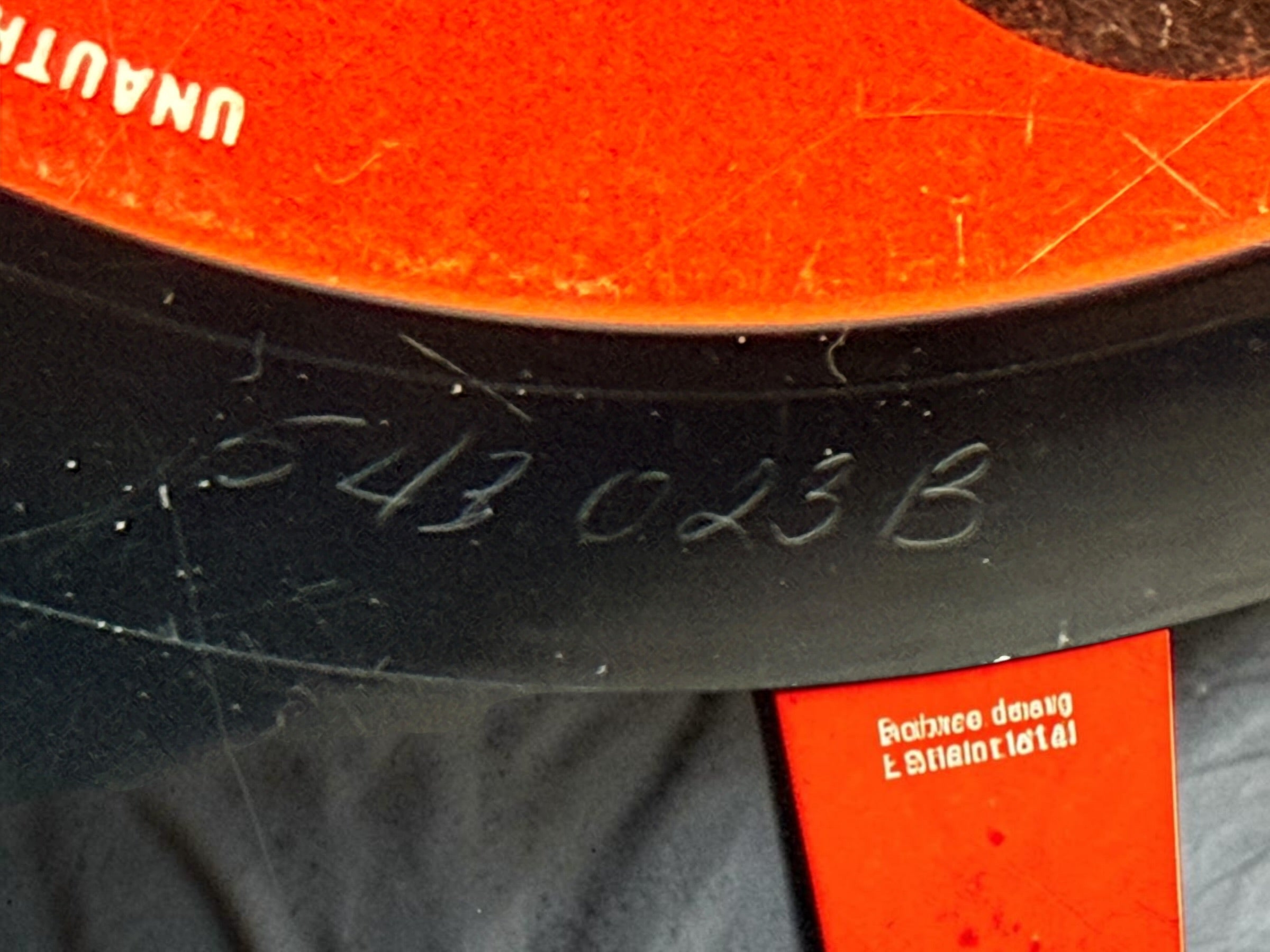 Close-up of a black tire sidewall with embossed serial numbers '543 023 B' and part of a bright orange label or packaging insert.