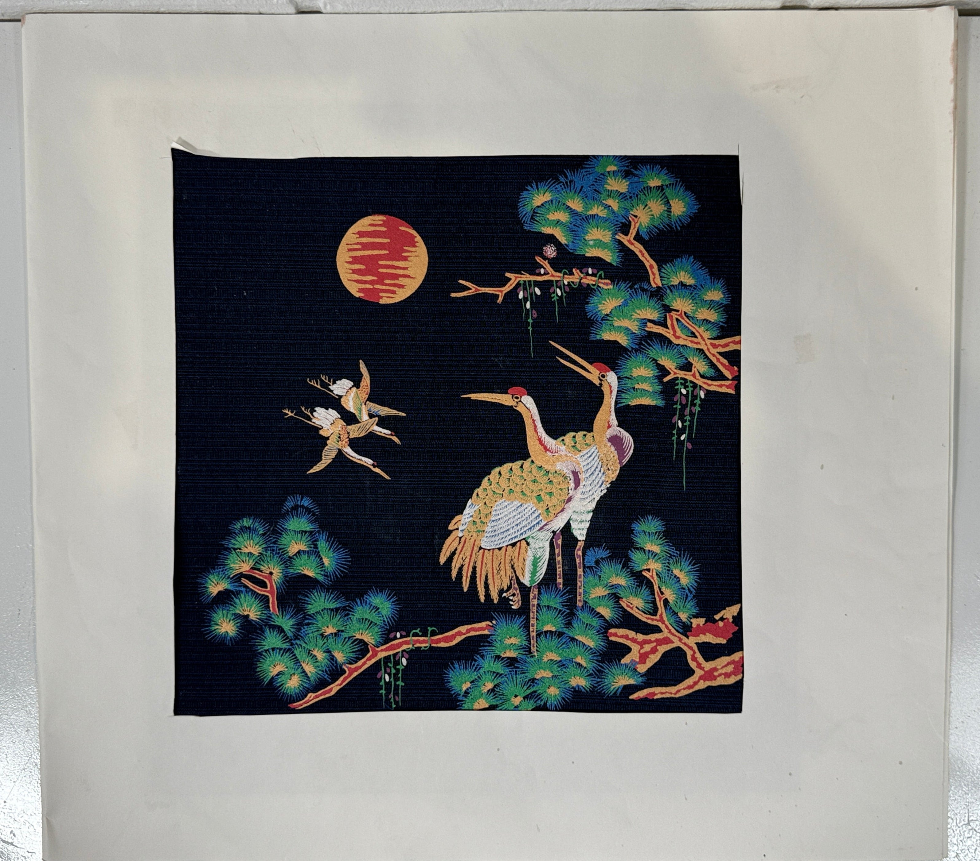 Embroidered artwork with cranes and a moon on a dark background, framed in a white frame.