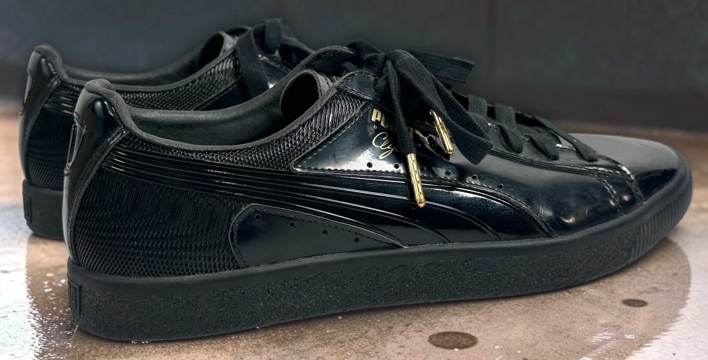 PUMA Clyde black patent-style men’s sneakers, US 10 / EU 43, featuring gold Clyde branding, tonal Formstrip and classic low-top styling.