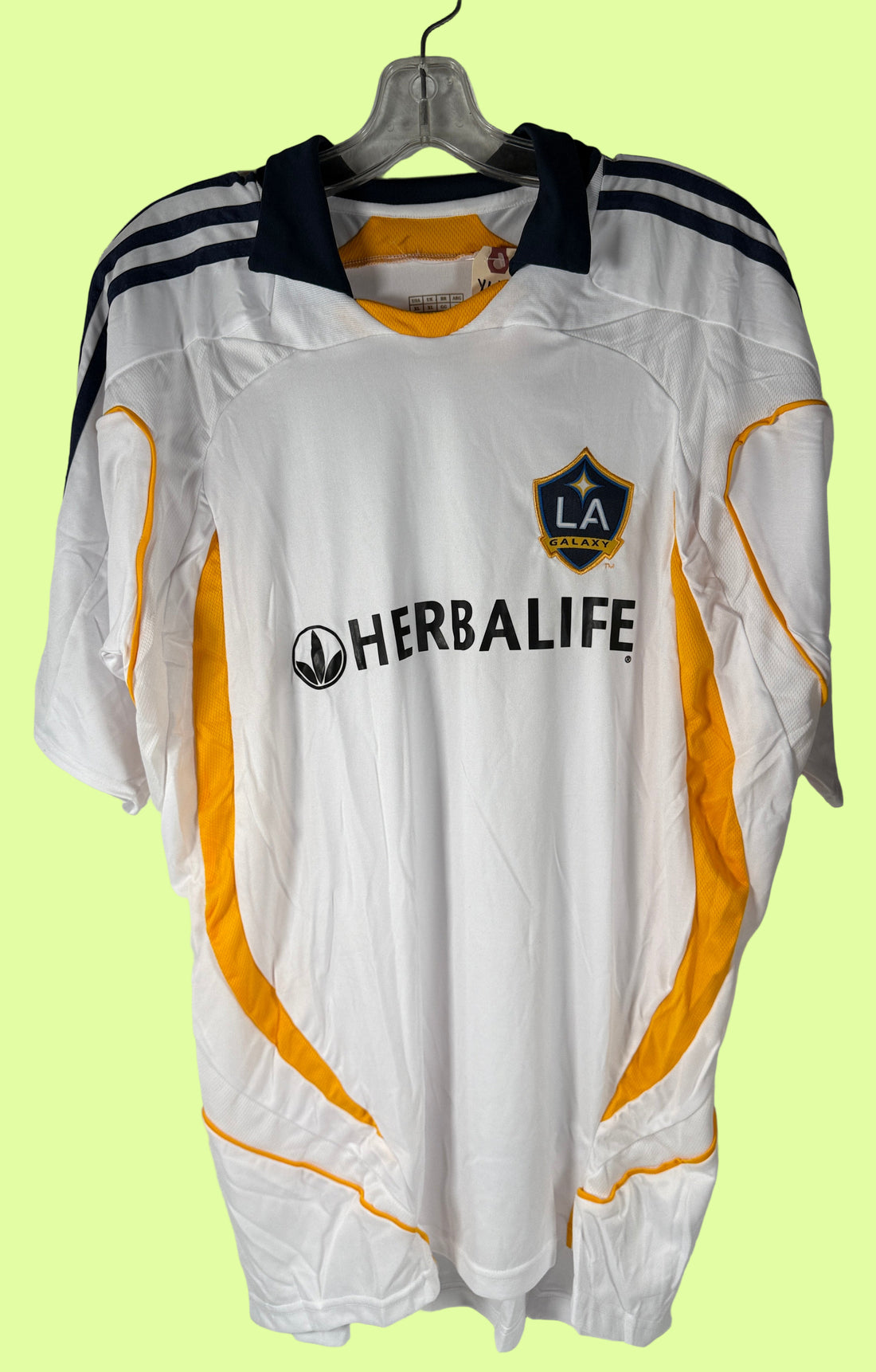 White sports jersey with yellow accents and Herbalife logo on a hanger against a tiled wall.
