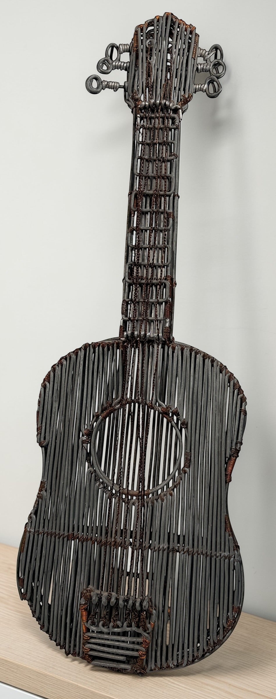 Vintage handmade wire guitar sculpture crafted from steel and copper. Industrial folk art decor piece with freestanding stand, perfect for music room or studio display.