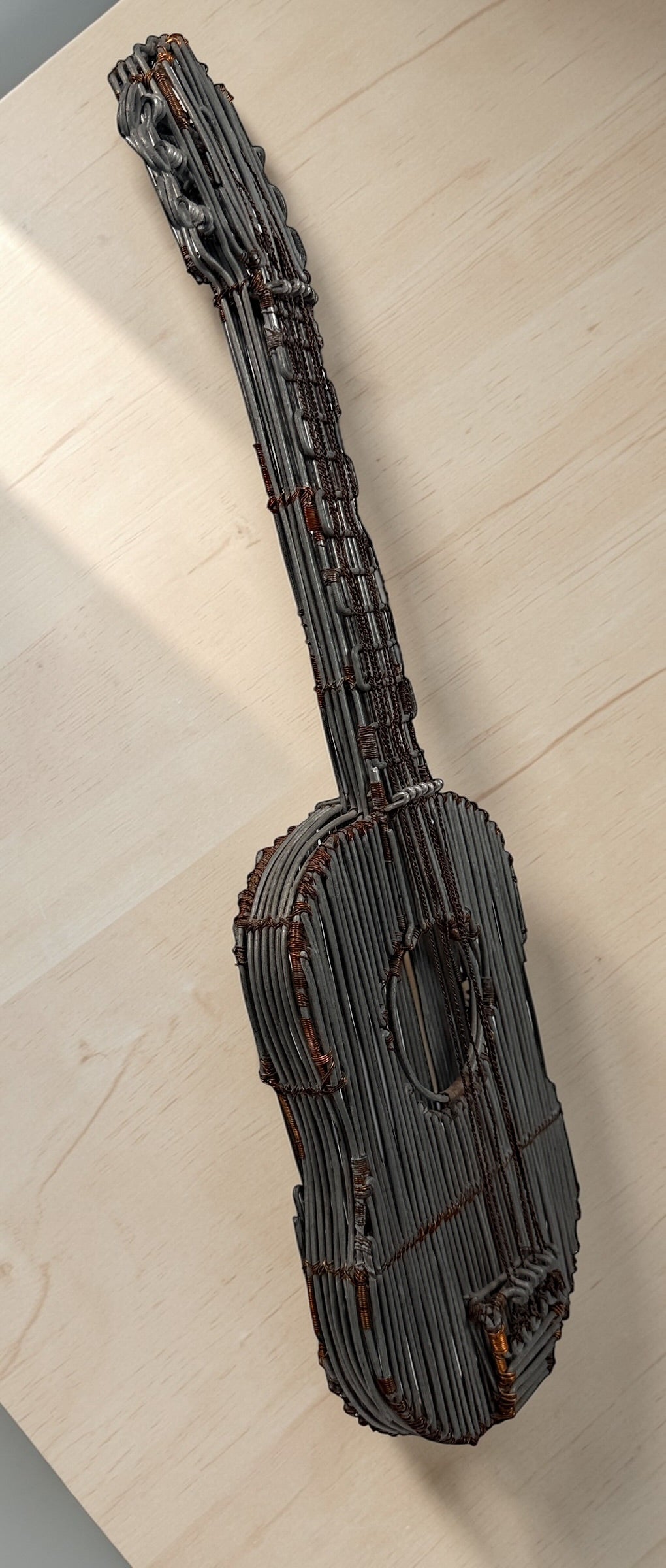 Vintage handmade wire guitar sculpture crafted from steel and copper. Industrial folk art decor piece with freestanding stand, perfect for music room or studio display.