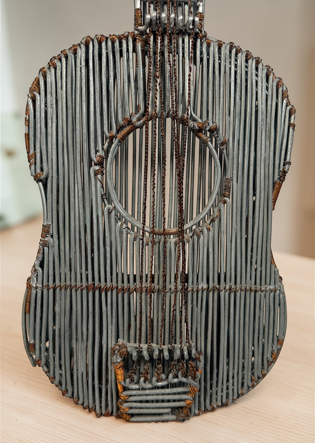 Vintage handmade wire guitar sculpture crafted from steel and copper. Industrial folk art decor piece with freestanding stand, perfect for music room or studio display.