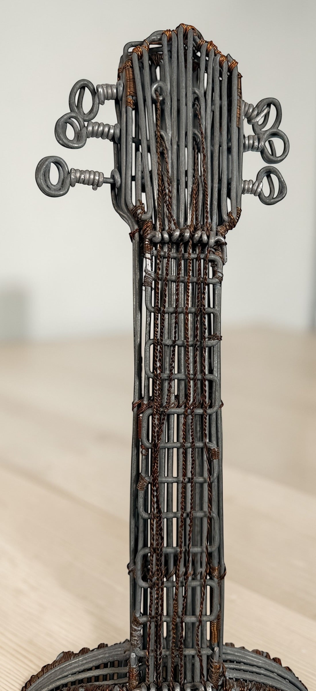 Vintage handmade wire guitar sculpture crafted from steel and copper. Industrial folk art decor piece with freestanding stand, perfect for music room or studio display.