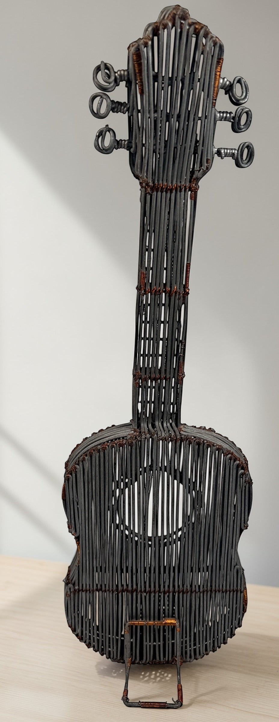 Vintage handmade wire guitar sculpture crafted from steel and copper. Industrial folk art decor piece with freestanding stand, perfect for music room or studio display.