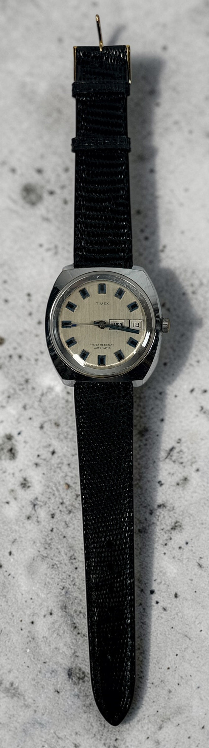 Vintage Timex automatic day-date watch with blue markers and 1970s cushion case design. Affordable mechanical wristwatch with classic retro style.