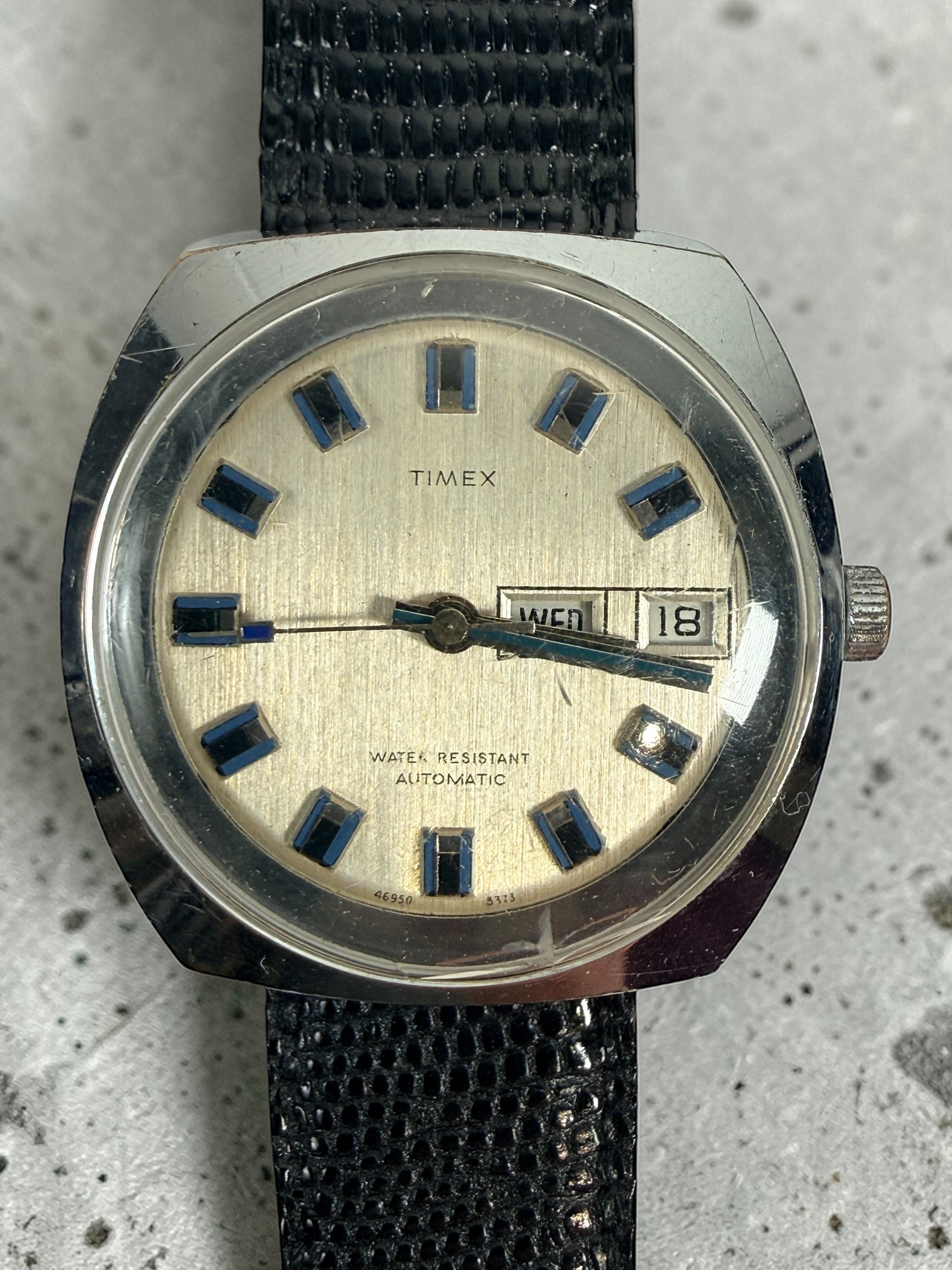 Vintage Timex automatic day-date watch with blue markers and 1970s cushion case design. Affordable mechanical wristwatch with classic retro style.