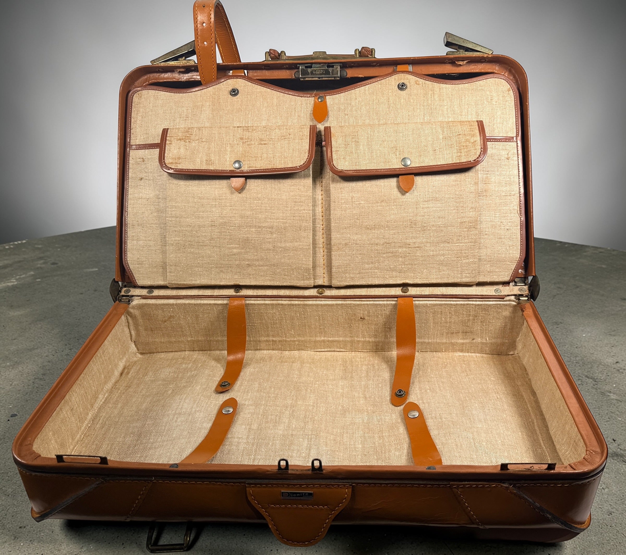 Vintage tan leather suitcase by Dionite Luggage. 1960s structured valise with brass hardware and interior compartments. Great for travel or decor.