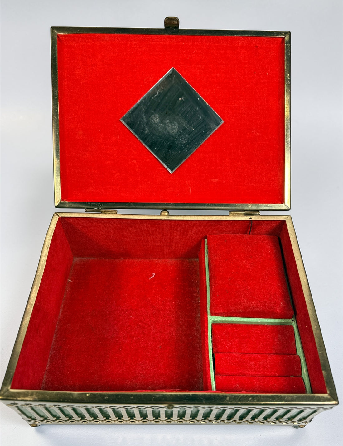 Vintage Mele Hollywood Regency jewelry box with brass filigree and green glass. Red velvet interior with compartments. Decorative mid-century piece.