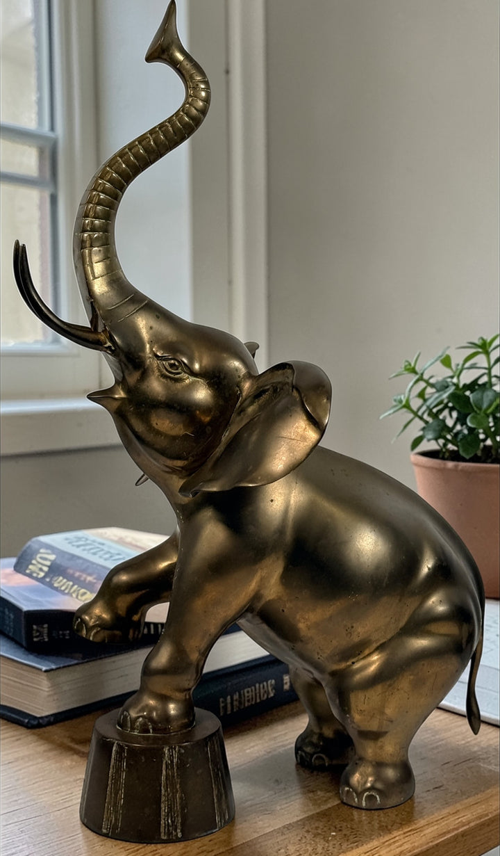Vintage brass elephant figurine in circus pose with raised trunk. Mid-century decor piece with patina, solid cast construction, and strong display presence.