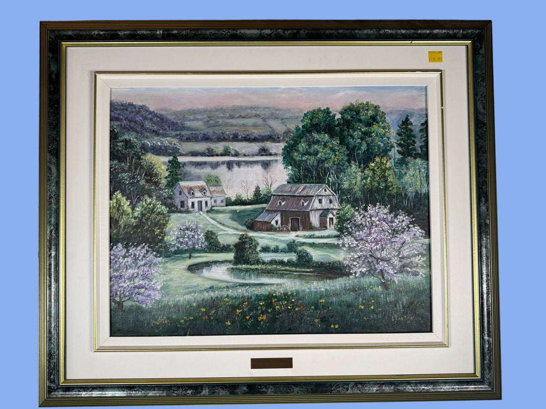 Framed painting of a landscape with houses and trees on a gray wall.