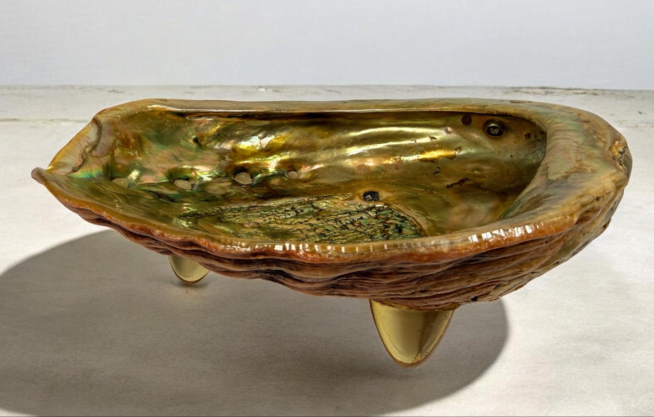 Vintage abalone shell bowl with lucite feet. Iridescent centerpiece dish for coastal, tiki, Hollywood Regency, and mid-century modern decor.