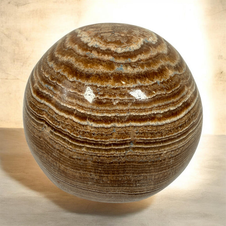 Vintage 4 inch banded onyx calcite sphere with rich honey and cream natural striping. Heavy polished stone décor piece for shelf, desk, or tabletop display.