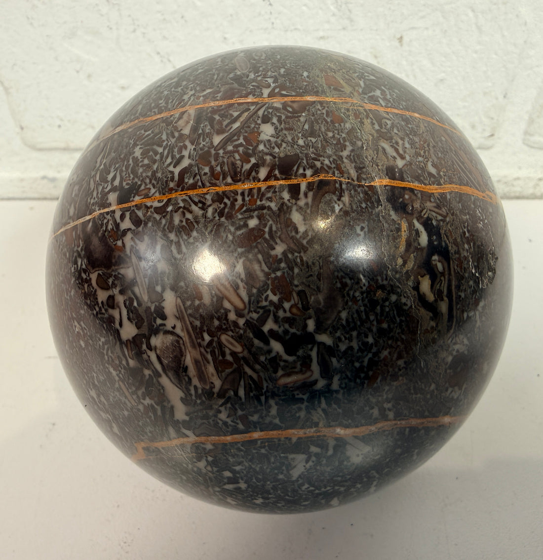 Large Orthoceras fossil sphere from Morocco with visible prehistoric shell fossils in polished black stone. Natural history décor collectible display piece.